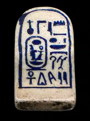 Photo d'une plaquette qui était attachée à un étui contenant des rouleaux de papyrus. La plaquette est en forme de stèle cintrée avec 2 colonnes de texte hiéroglyphique portant le nom du pharaon Aménophis 3.